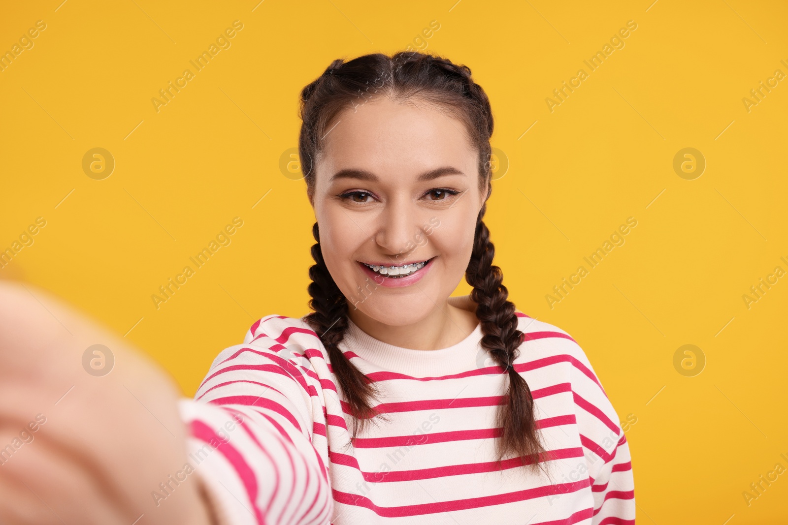 Photo of Smiling woman with braces taking selfie on orange background