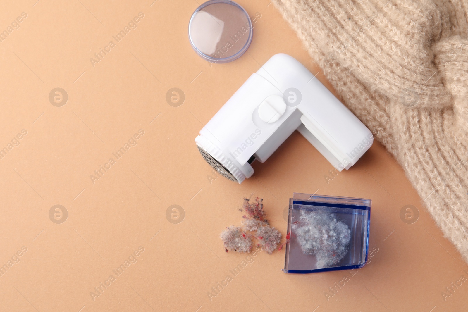 Photo of Modern fabric shaver with fuzz and knitted headdress on pale orange background, flat lay. Space for text