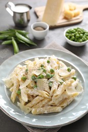 Photo of Delicious pasta with green peas, cheese, creamy sauce and ground pepper on grey table