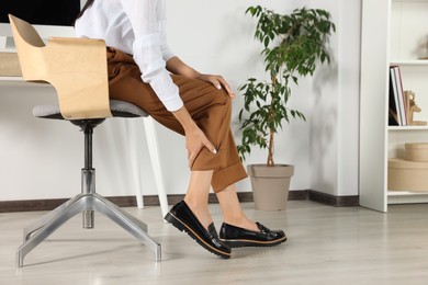 Photo of Woman rubbing sore leg in office, closeup