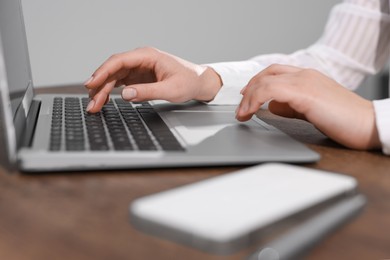 Photo of Woman with smartphone and pen working on laptop at wooden table, closeup. Electronic document management