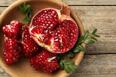 Cut fresh pomegranate and green leaves on wooden table, top view