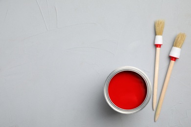 Open can with red paint and brushes on grey background, flat lay. Space for text