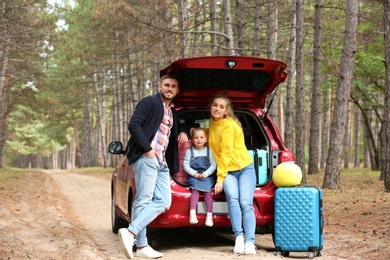 Photo of Happy young family near car trunk loaded with suitcases outdoors