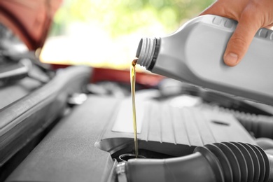 Photo of Mechanic pouring oil into car engine, closeup