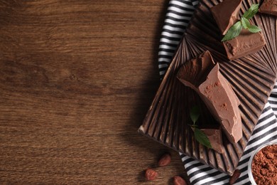 Pieces of tasty milk chocolate, cocoa beans, powder and mint on wooden table, top view. Space for text