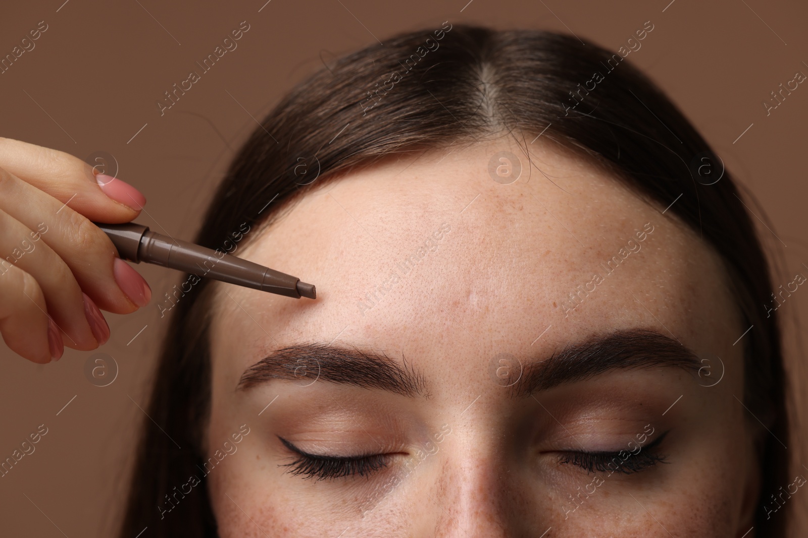Photo of Beautiful woman drawing freckles with pen on brown background, closeup