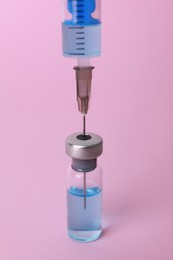 Disposable syringe with needle and vial on pink background, closeup