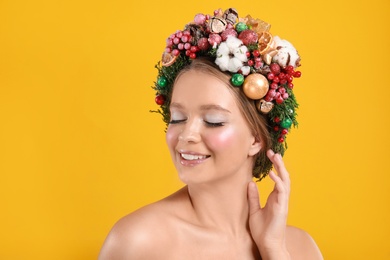 Photo of Beautiful young woman wearing Christmas wreath on yellow background