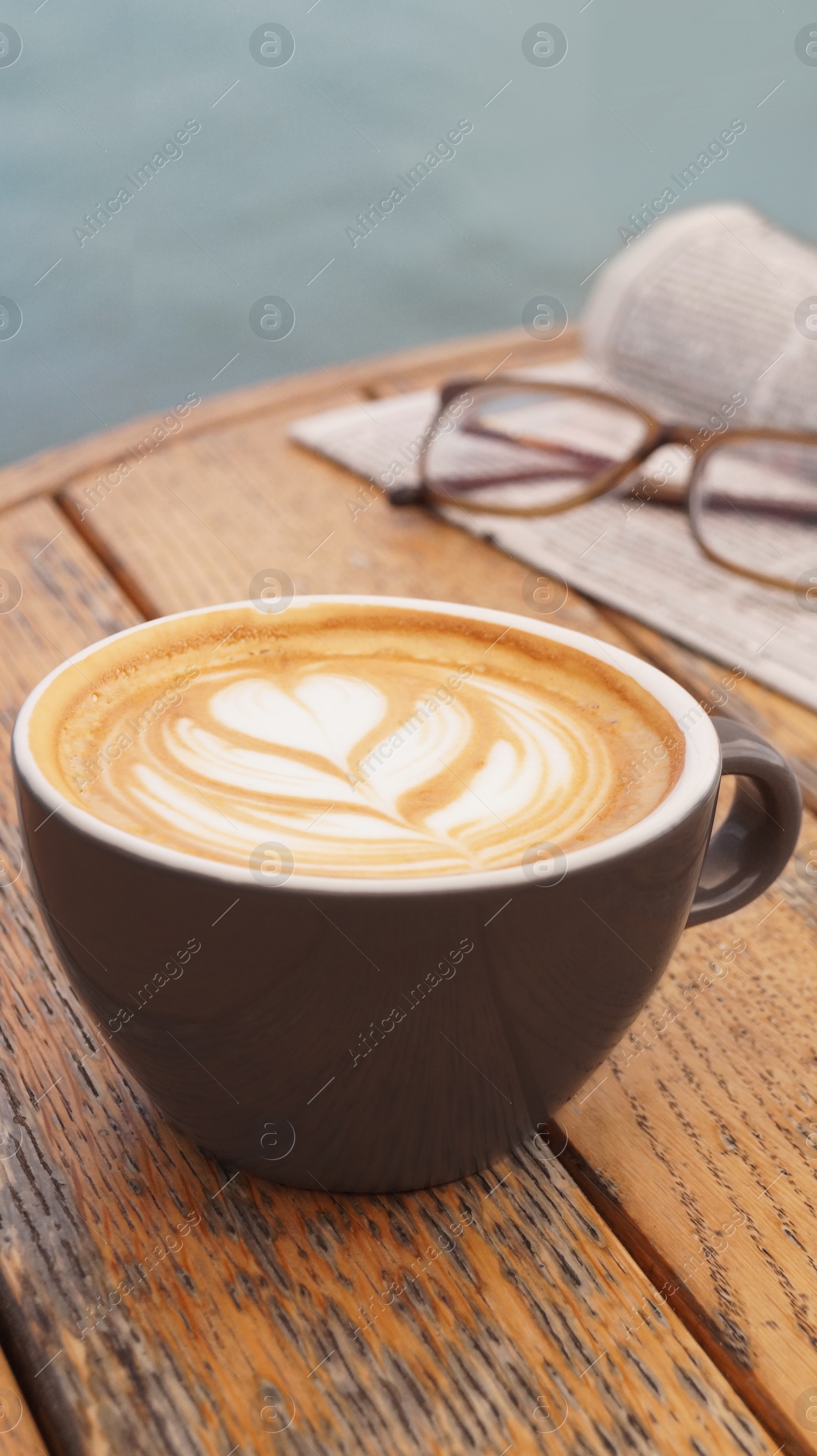 Photo of Cup of delicious coffee, eyeglasses and newspaper on wooden table