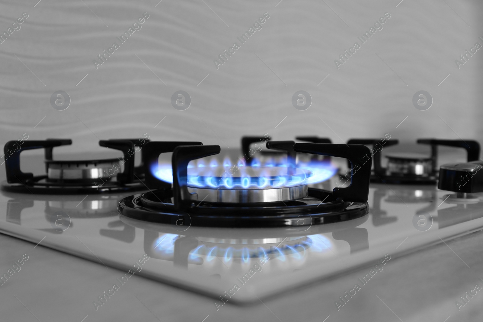 Photo of Modern gas cooktop with burning blue flame in kitchen
