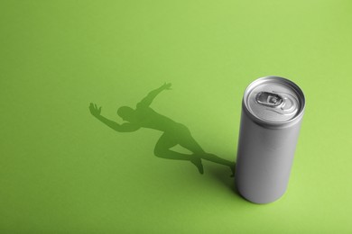 Energy drink and shadow in shape of sportsman's silhouette on light green background 