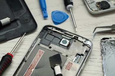 Photo of Parts of damaged smartphone and repair tools on light beige wooden table, closeup