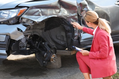 Insurance agent filling claim form near broken car outdoors