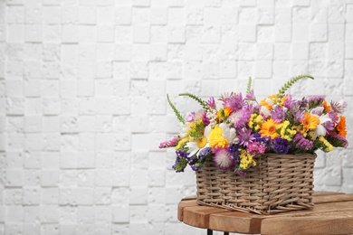 Wicker basket with beautiful wild flowers on table near white wall