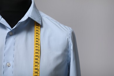Photo of Semi-ready shirt with tailor's measuring tape on mannequin against grey background, closeup. Space for text