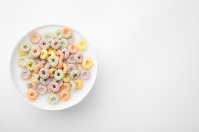 Tasty colorful cereal rings and milk in bowl on white background, top view. Space for text