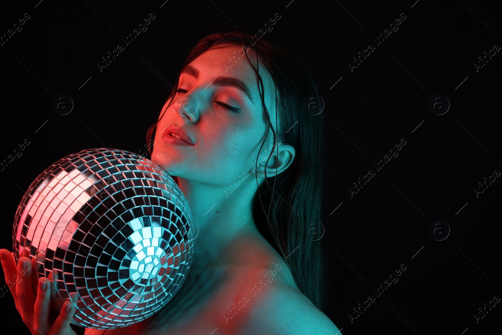 Photo of Beautiful woman with disco ball posing in neon lights against black background. Space for text