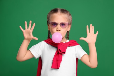 Photo of Girl in sunglasses blowing bubble gum on green background