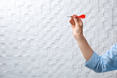 Woman holding dart against light wall. Business trainer concept