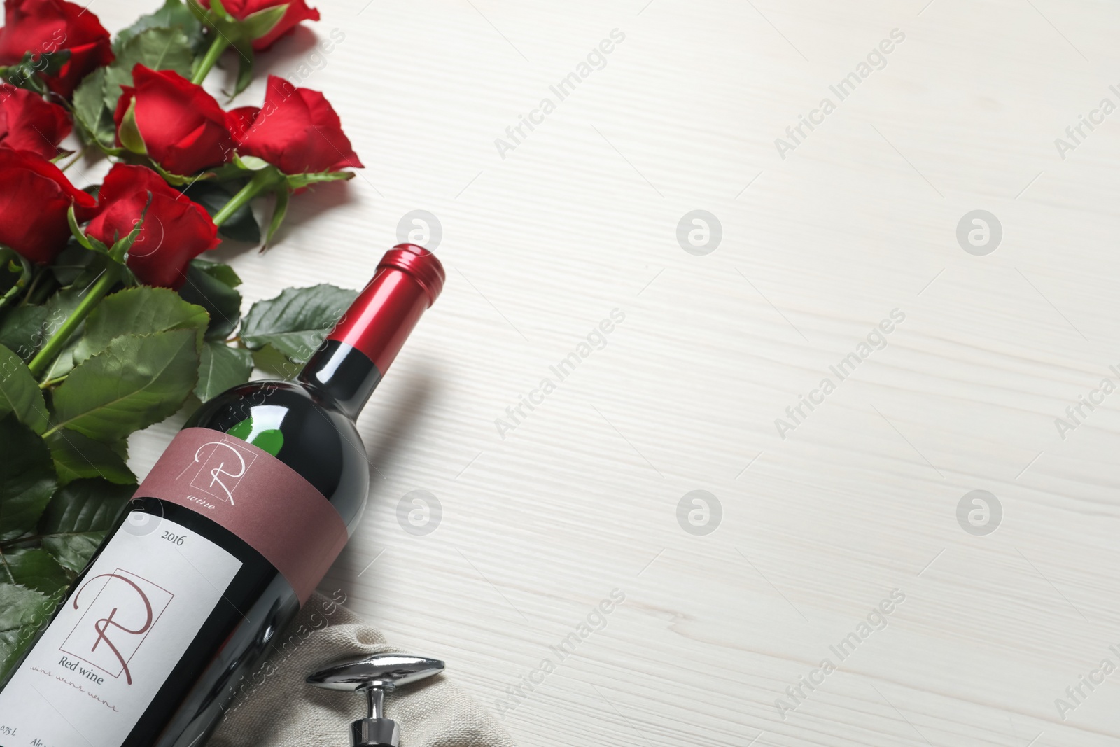 Photo of Bottle of red wine and beautiful roses on white wooden table. Space for text