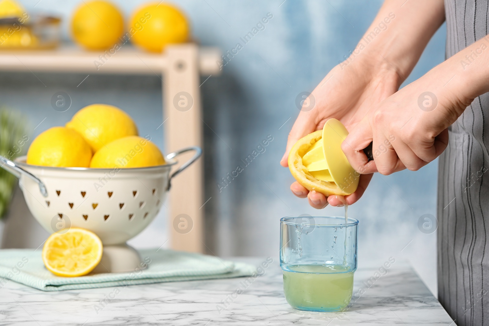 Photo of Woman squeezing lemon juice with reamer into glass on table