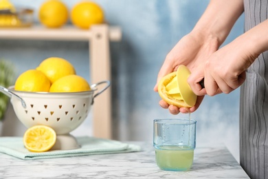 Photo of Woman squeezing lemon juice with reamer into glass on table