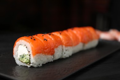 Photo of Tasty sushi rolls with salmon, cream cheese and cucumber on black wooden table, closeup