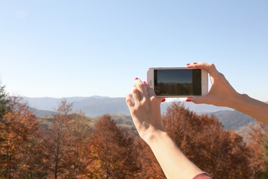 Woman taking photo of beautiful mountain landscape with smartphone