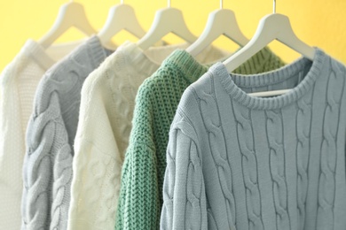 Collection of warm sweaters on yellow wall, closeup