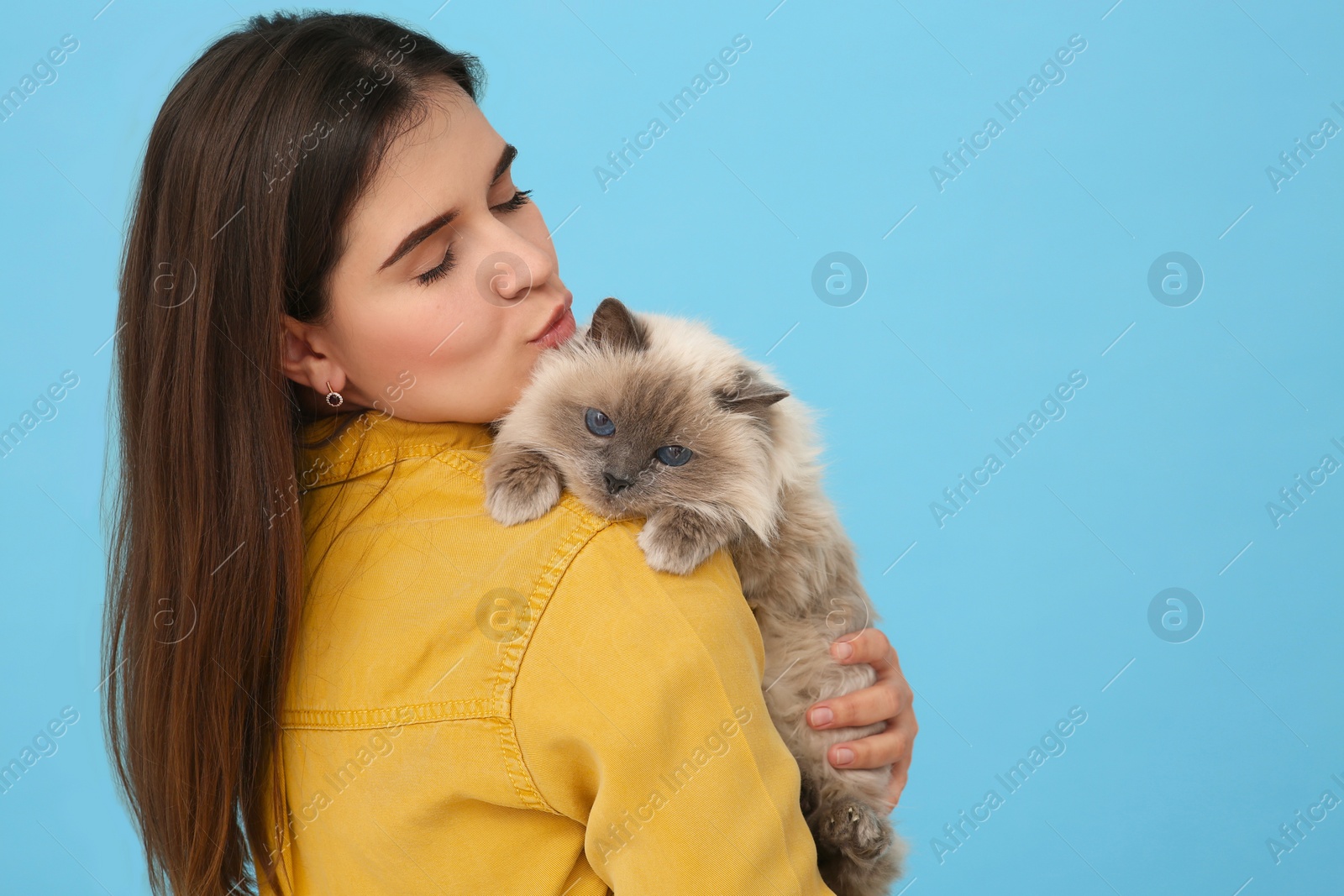 Photo of Woman kissing her cute cat on light blue background, space for text