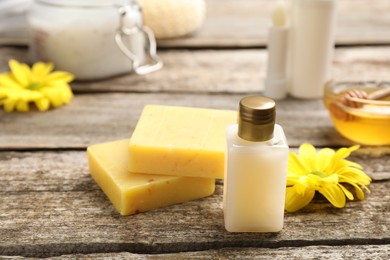 Photo of Bottle of cosmetic product and natural beeswax on wooden table