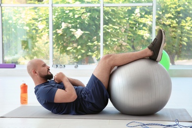 Photo of Overweight man doing exercise with fitness ball in gym