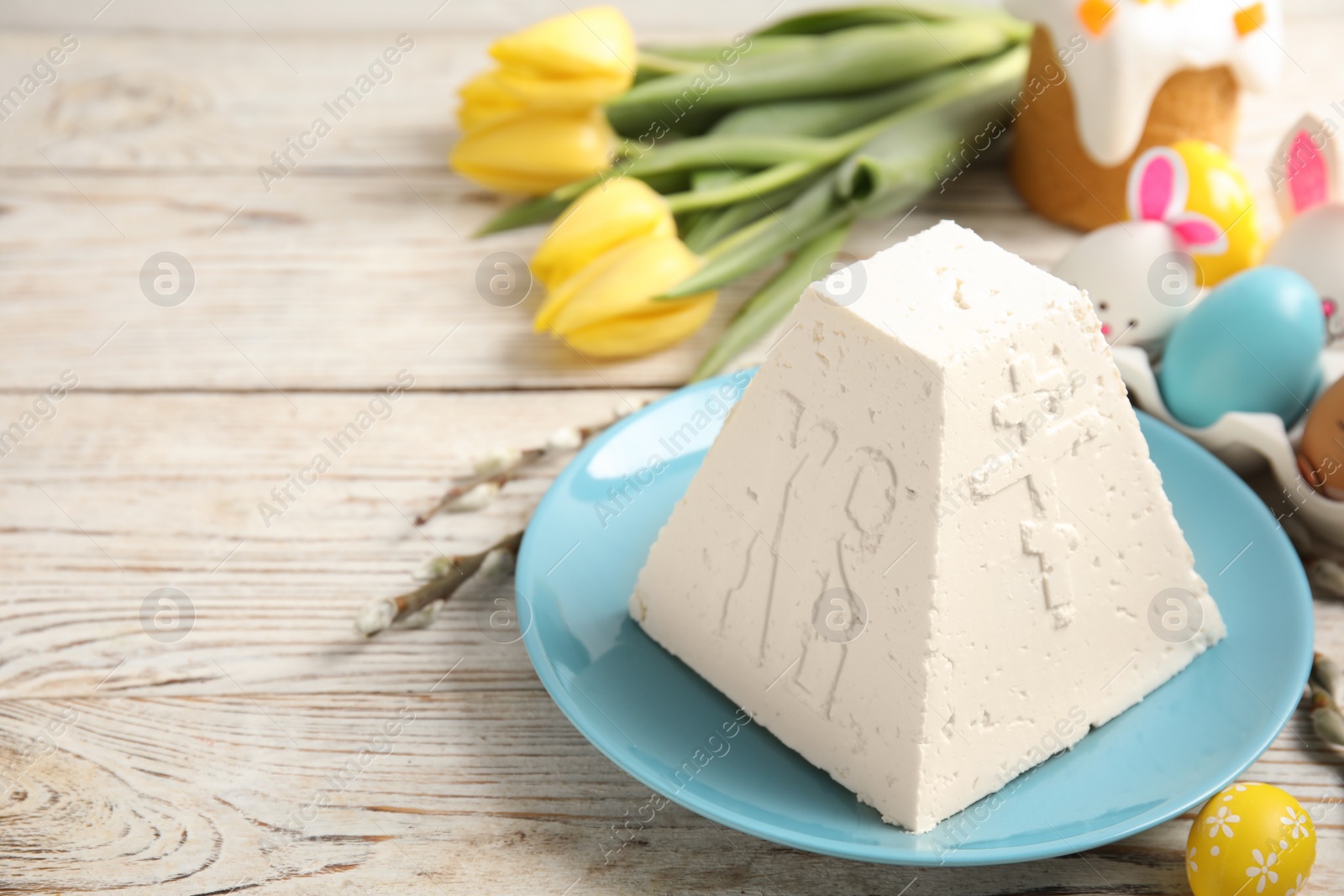 Photo of Traditional cottage cheese Easter paskha and dyed eggs on white wooden table, space for text