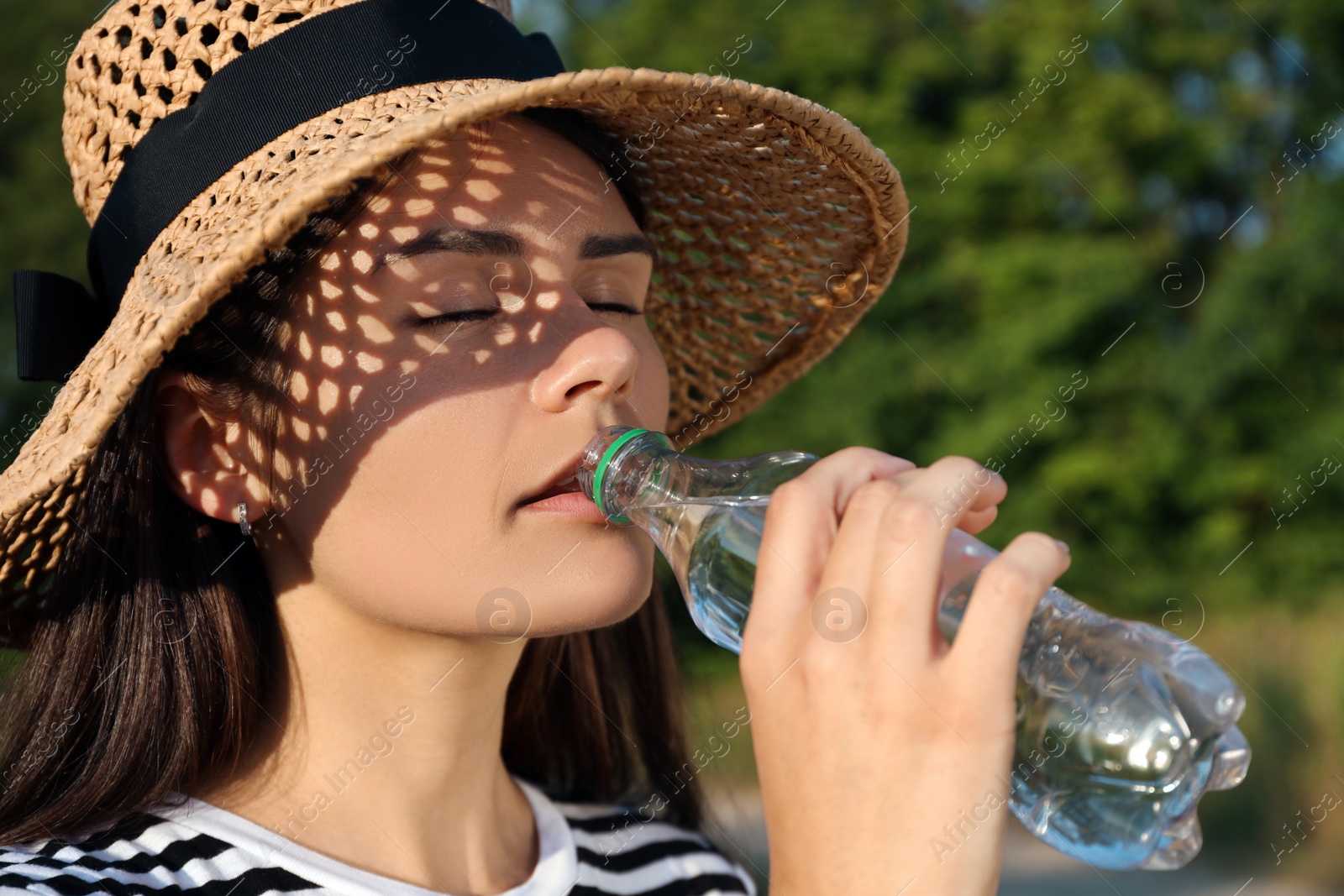 Photo of Young woman in straw hat drinking water outdoors on hot summer day. Refreshing drink