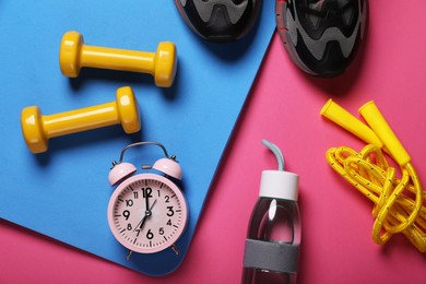 Photo of Alarm clock, bottle of water and sports equipment on pink background, flat lay. Morning exercise