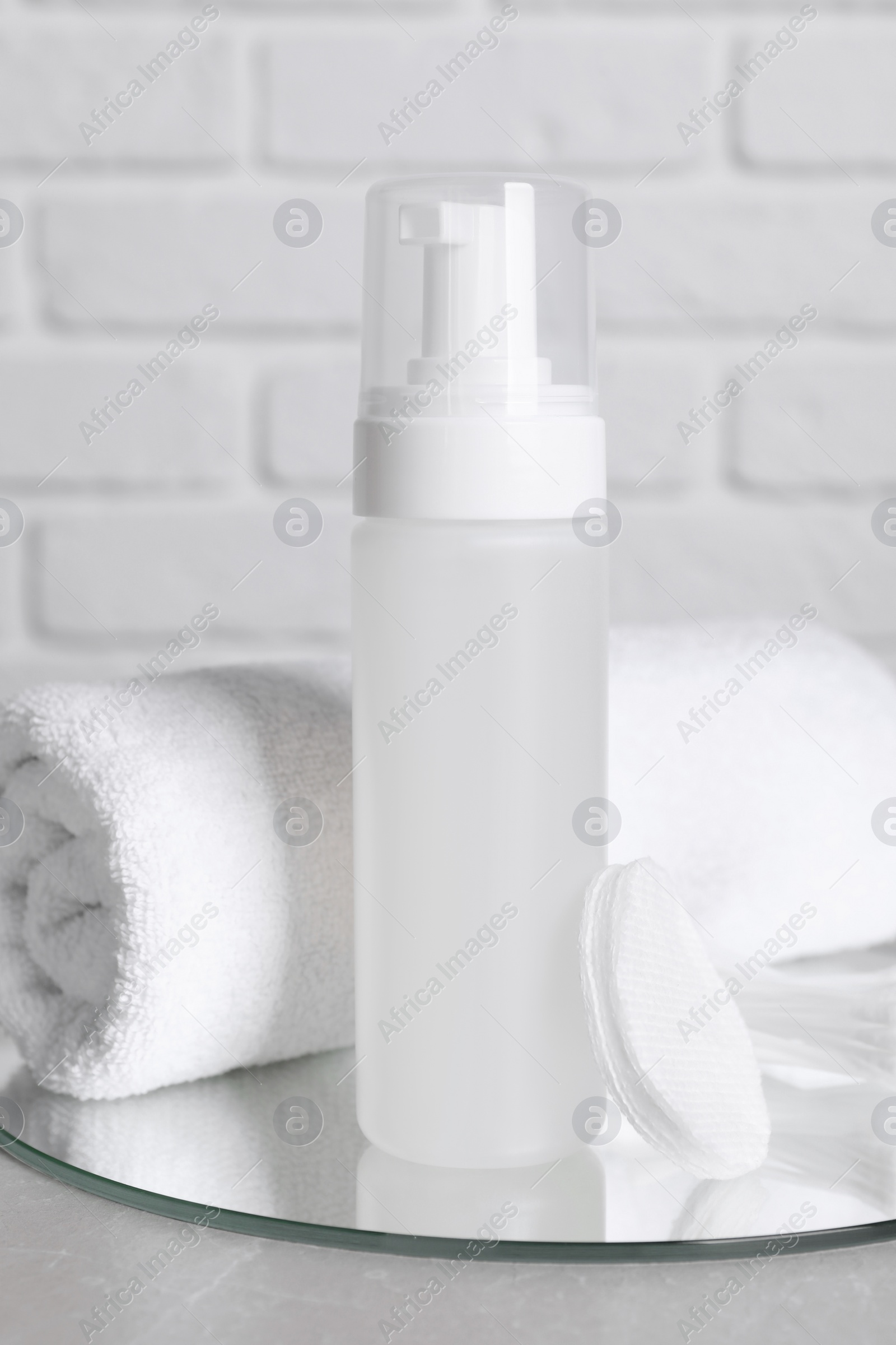 Photo of Bottle of face cleansing product, towel and cotton pads on grey table. Space for text