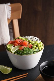 Photo of Delicious poke bowl with lime, fish and edamame beans on black table