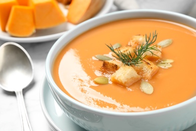 Photo of Tasty creamy pumpkin soup with croutons, seeds and dill in bowl on table, closeup