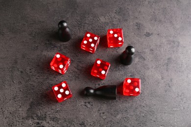 Photo of Many red dices and black game pieces on grey textured table, flat lay