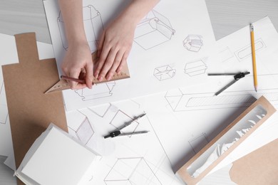 Woman creating packaging design at light wooden table, top view