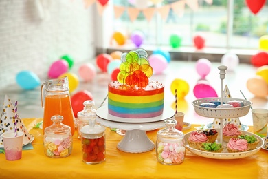 Photo of Bright birthday cake and other treats on table in decorated room