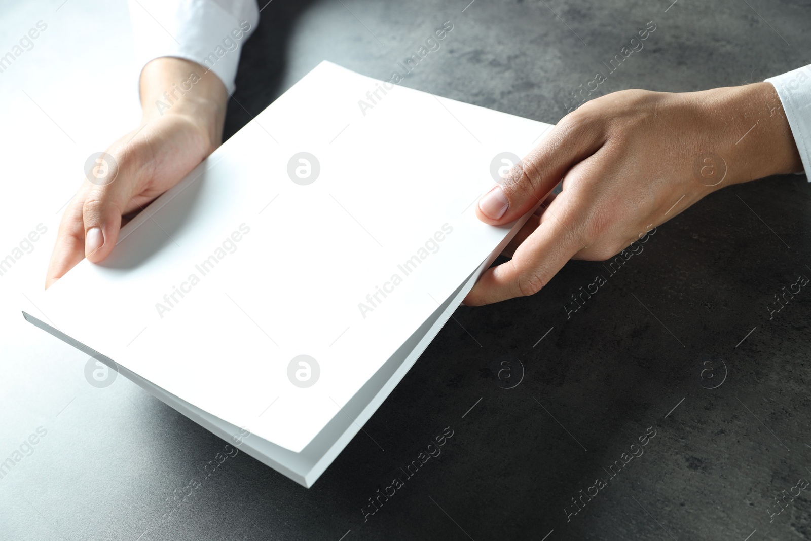 Photo of Man holding blank notebook at black textured table, closeup. Mockup for design