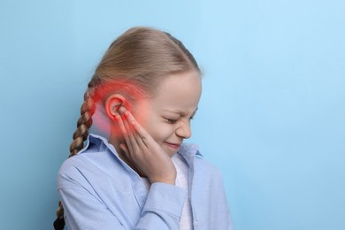 Image of Little girl suffering from ear pain on light blue background, space for text