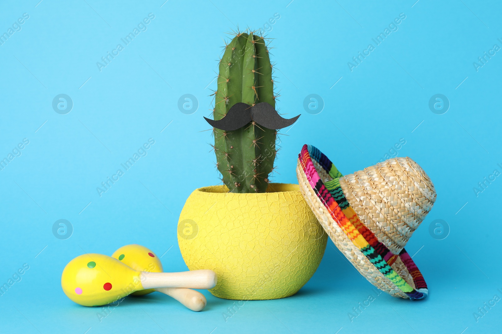 Photo of Mexican sombrero hat, cactus with fake mustache and maracas on light blue background