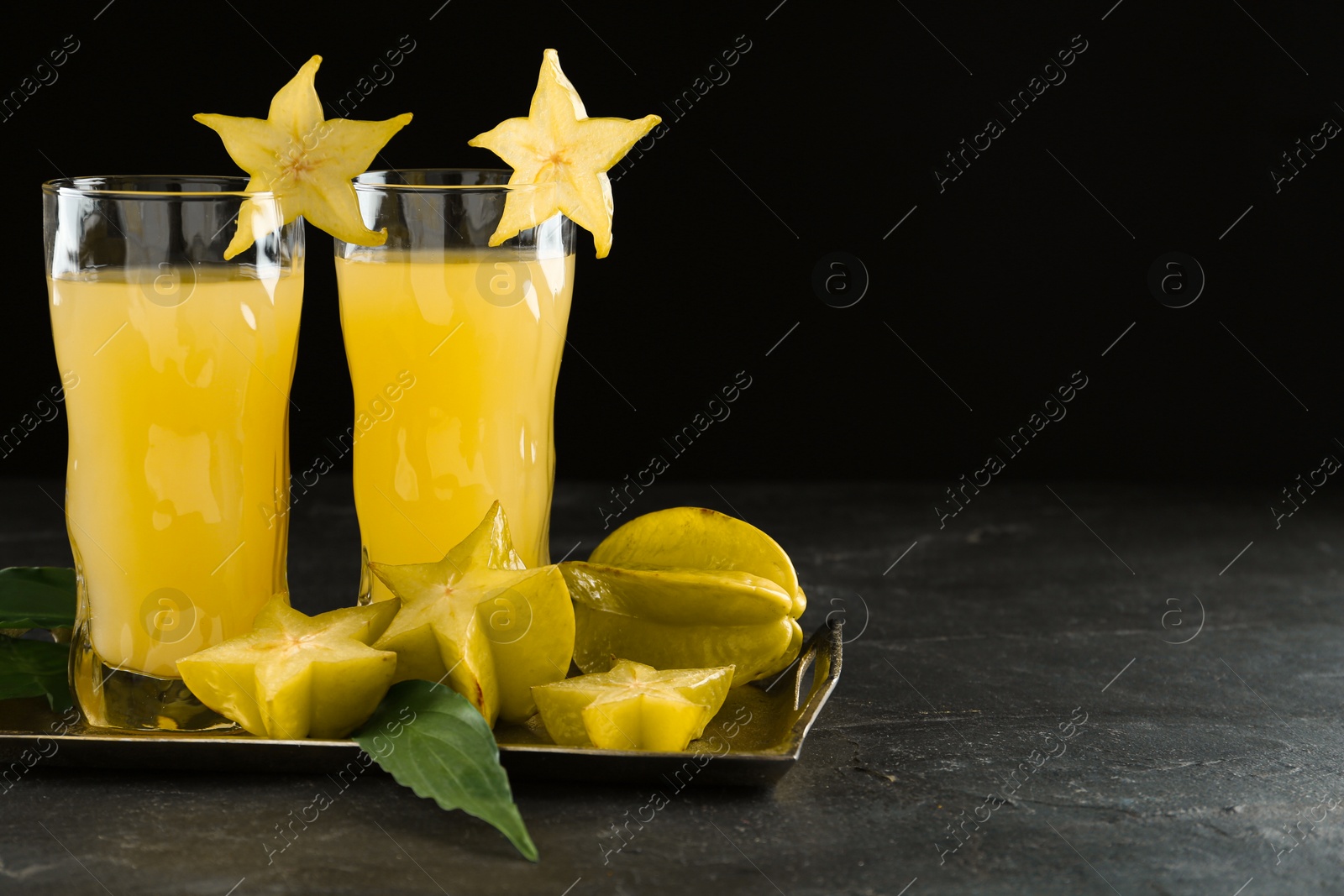 Photo of Delicious carambola juice in glasses on black table. Space for text