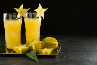 Delicious carambola juice in glasses on black table. Space for text