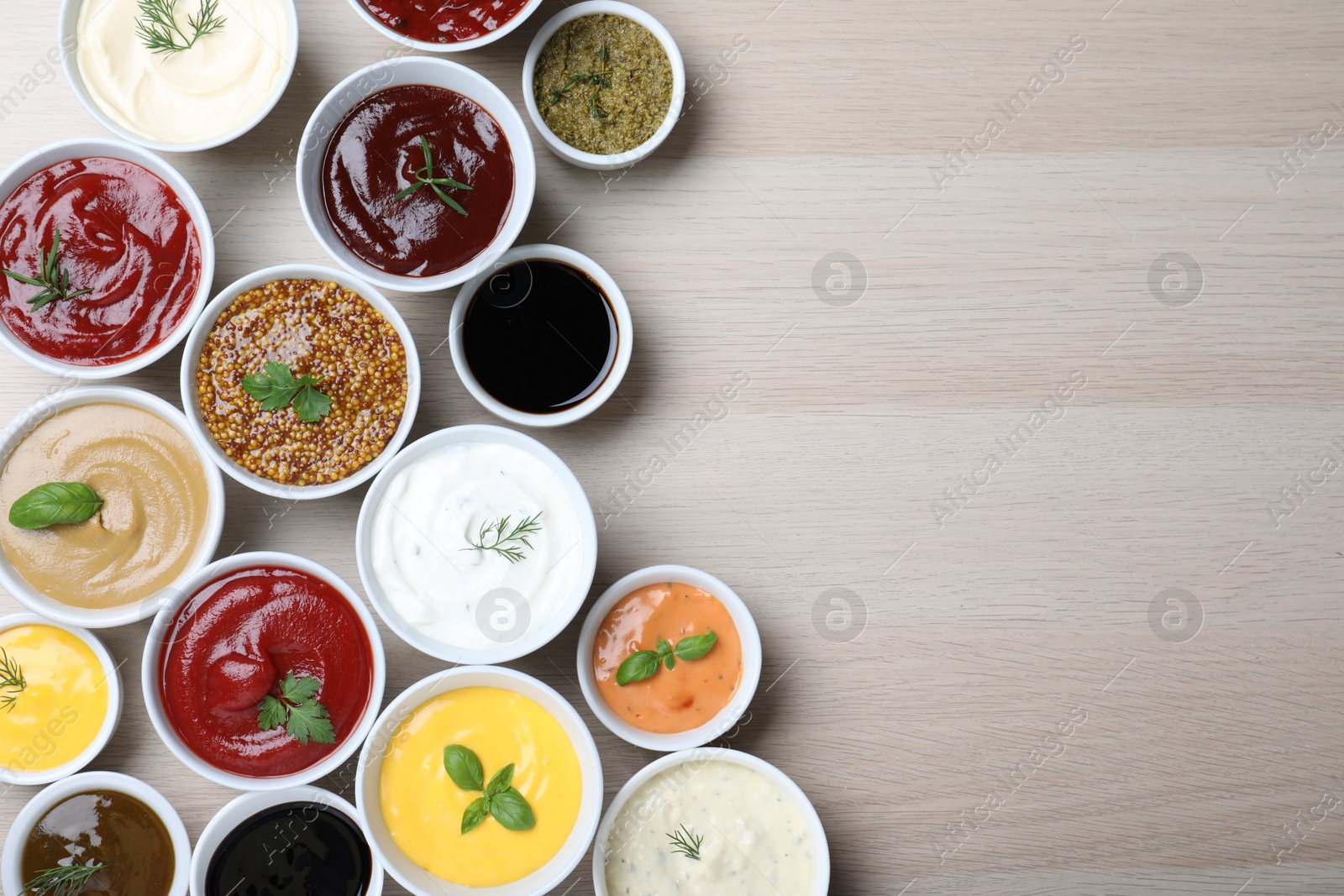 Photo of Many different sauces and herbs on wooden table, flat lay. Space for text
