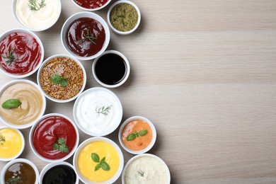 Many different sauces and herbs on wooden table, flat lay. Space for text