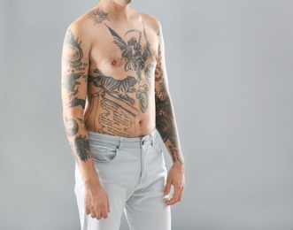 Young man with stylish tattoos on grey background